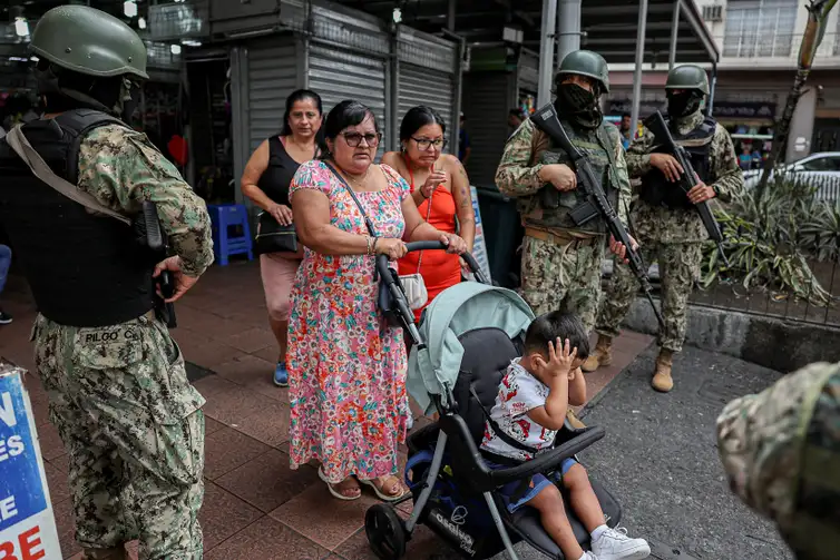 Reuters/IVAN ALVARADO People walk past armed soldiers, as they guard a commercial area, in the aftermath of a wave a violence that saw the storming of a TV station on-air and explosions around the nation, in Quito, Ecuador, January 11, 2024. REUTERS/Ivan Alvarado