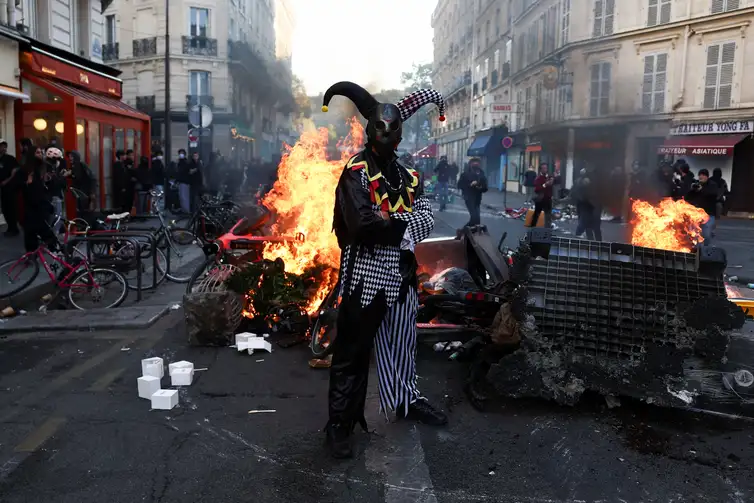 A demonstrator wearing a costume stands in front of burning flames, in Paris, France, October 18, 2026. REUTERS/Abdul Saboor